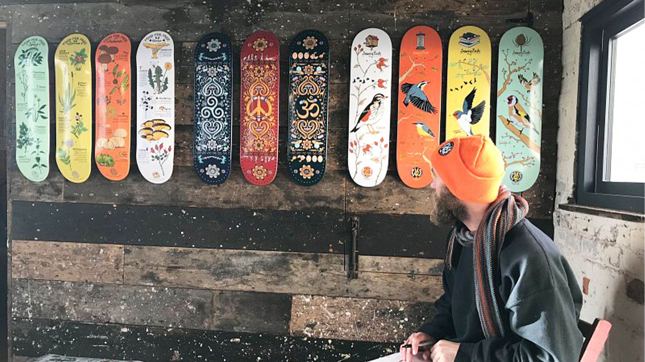 An artist sitting with his range of illustrated skateboards.